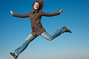 Girl in coat and jeans in jump against blue sky. In bright autumn day.