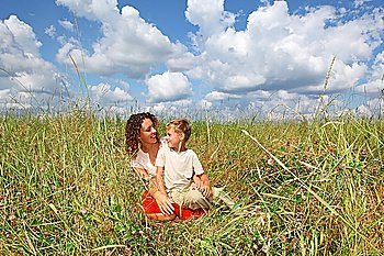 young woman and smiling boy sitting on meadow, Looking against each other