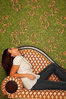 Girl in jeans sits on sofa and looks at wall with patten wall-paper