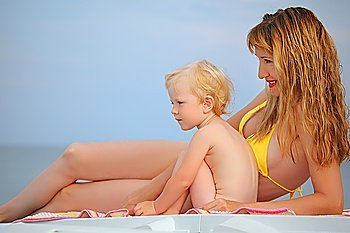 beautiful woman with blond  little baby girl lying on beach, looking afar