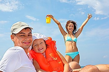young man with little girl in orange lifejacket and beautiful woman with plastic toy bucket, woman lifted hands upwards