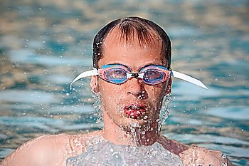 young man in watersport goggles swimming in pool, Aome up from water