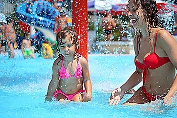 Smiling beautiful woman and little girl bathes in pool under water splashes