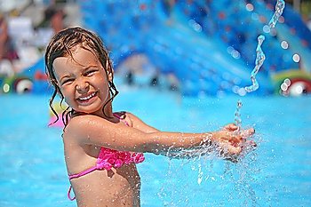 little girl bathes in pool under water splashes in aquapark
