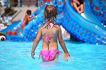 little girl standing in pool in aquapark, standing back