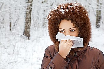 young woman with scarf blowing nose in wood in winter
