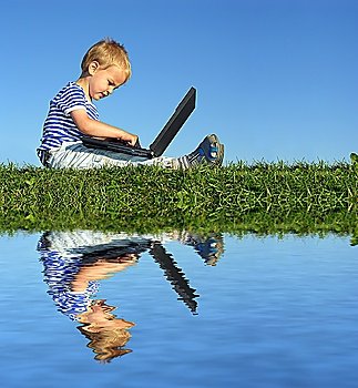 Young boy on laptop by lake