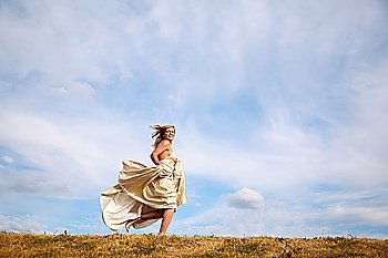young woman in the dress runs along the meadow