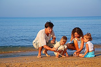 Parents play with children finding shells on sand at edge of sea