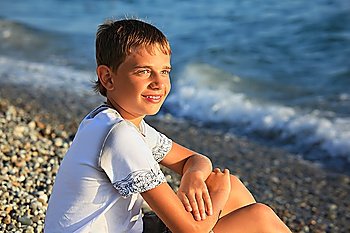 sitting teenager boy on stone seacoast