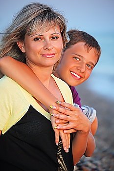 smiling boy embraces young woman on beach in evening