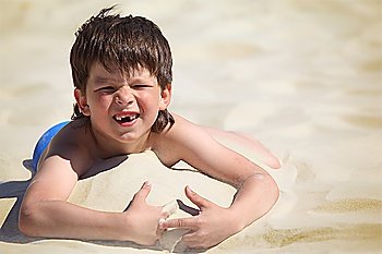 boy without  foreteeth lies on sand
