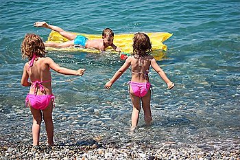 boy on inflatable mattress in sea and two girls nearby