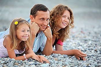 Happy family with little girl lying on stony beach