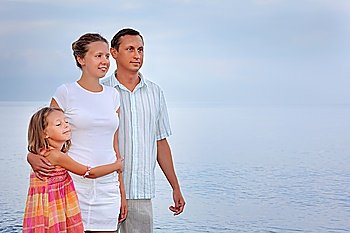 Happy family with little girl standing on beach in evening