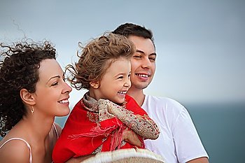 young man and beautiful woman protects little girl from wind on seacoast
