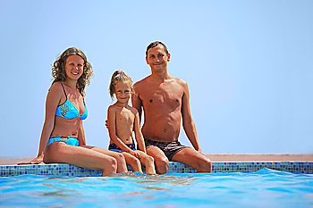 parents and daughter sit at edge of pool