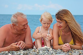 Mother and grandfather with child lie on sea coast