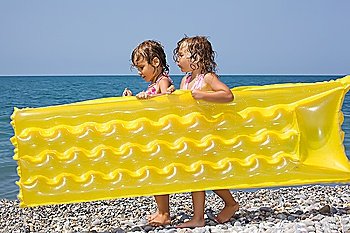 two pretty little girls bearing in hands inflatable mattress on beach