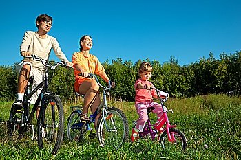 The father, mum and daughter go for a drive a sunny day on bicycles.