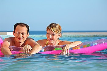 young man and nice women lying on an inflatable mattress in pool