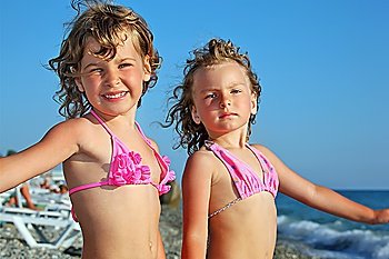 two pretty little girls on beach near sea, placed hands in sides