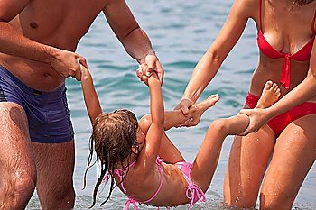 young family bathes in sea. wet happy daddy and mum play with daughter standing in water