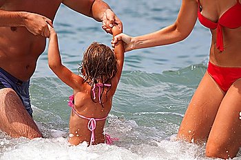 young family bathes in sea. wet happy daddy and mum play with daughter standing in water. Parents hold child for hands
