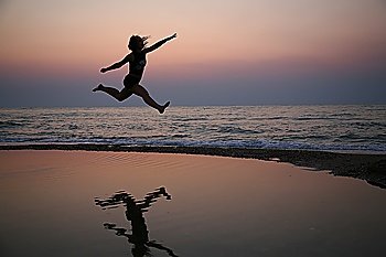 Young woman jumps on beach on sunset 