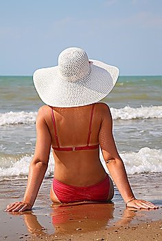 young woman sits on the sand on the edge of the sea