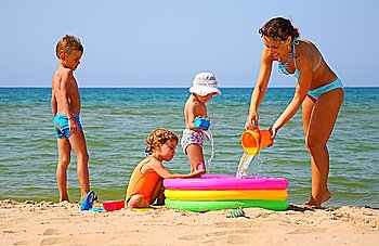 Mother with children to pour water in inflatable pool on shore of sea