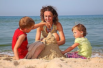 mother with children playing with sand on beach