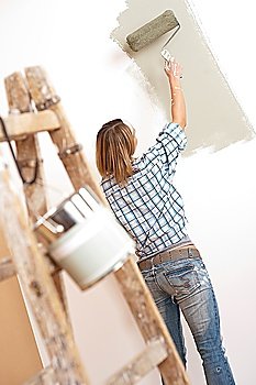 Home improvement: Cheerful woman with paint roller and ladder painting wall