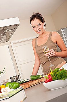 Smiling young woman cooking and holding glass of white wine