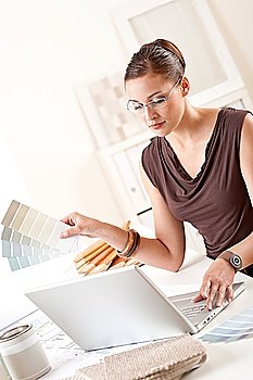 Smiling female designer with color swatch and laptop at office
