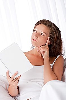 Woman thinking while reading book on sofa