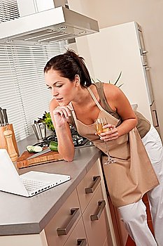 Woman with glass of white wine and laptop in the kitchen cooking