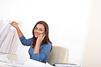 Female architect on the phone sitting at the office holding plans