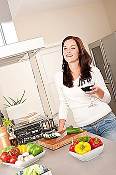 Smiling young woman with glass of red wine in the kitchen