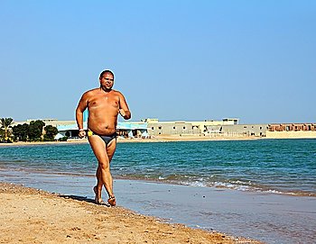 sport - overweight man running on sea coastline