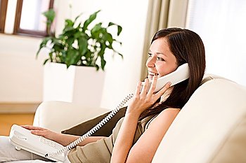 On the phone home: Young woman calling sitting on sofa in lounge