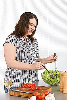 Cook - Plus size happy woman preparing vegetable salad with lettuce in modern kitchen