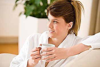 Young woman in white bathrobe with coffee in lounge