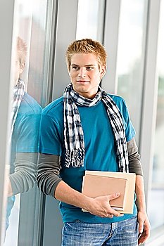 Male teenager read book standing in modern glass building