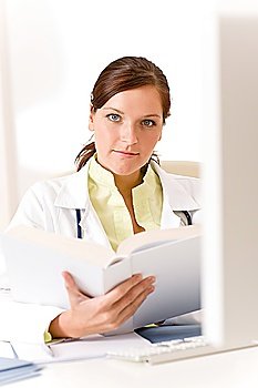 Female doctor read book in clinic sitting at desk