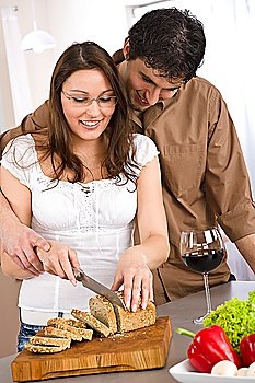 Happy couple cut bread in modern kitchen together and drink red wine