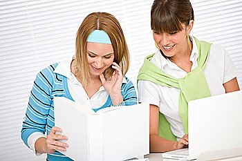 Student at home - two young woman study together with book and laptop