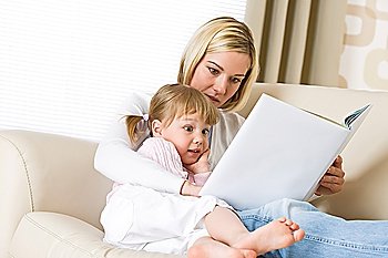 Mother with surprised little girl read book together in lounge