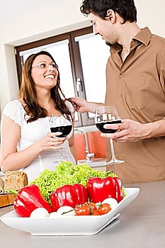 Happy couple drink red wine in modern kitchen, focus on vegetable