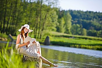 Long red hair romantic woman relax by lake with book on sunny day